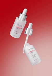 Due bottiglie di vetro opaco di siero all'acido azelaico al 12% TIRTIR con pipette, una aperta con una goccia che cade, su sfondo a gradiente rosso.