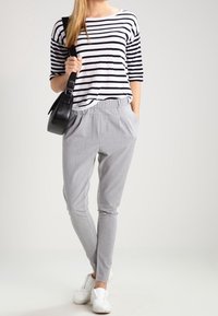 Maglietta a righe bianche e nere a maniche corte abbinata a pantaloni grigi chiaro a gamba stretta. Il modello indossa sneakers bianche e porta una borsa nera.