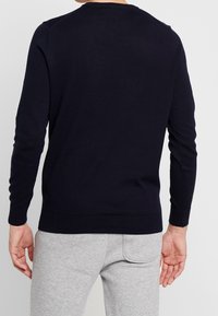 Mörkblå stickad tröja med rundad halsringning, ribbade ärmslut och nederkant; slät yta synlig; bärs med ljusgrå byxor.