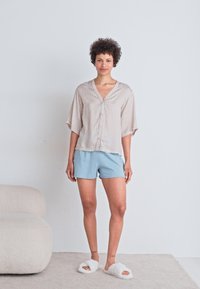 Lichtroze, geblokte blouse met korte, brede mouwen, gecombineerd met lichtblauwe shorts en witte, pluche slippers. Glad stofoppervlak.
