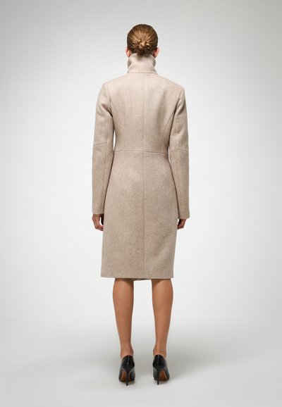 Beige uldfrakke med høj krave, slim fit og knælangt design. Har enkel syning og ingen synlige lukninger.