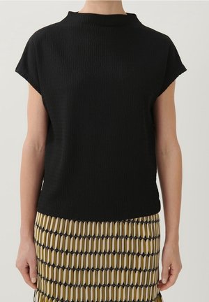 Vrouw draagt een zwart textuur kort mouw shirt gecombineerd met een patroonrokken met verticale gele en zwarte strepen.