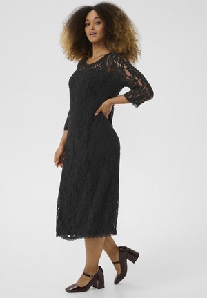 Black lace dress with three-quarter sleeves, scalloped hem, and a fitted design. Worn with glossy burgundy block-heeled shoes.