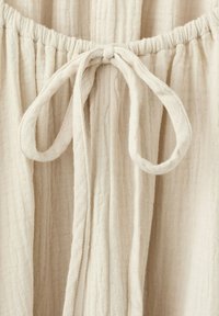 Gros plan sur un tissu en lin beige avec une taille élastiquée froncée et un nœud de cordon noué au centre devant.