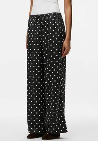 Melni, plati bikses ar auklu viduklī, ar baltu punktiņu rakstu un gludu, spīdīgu auduma tekstūru.
