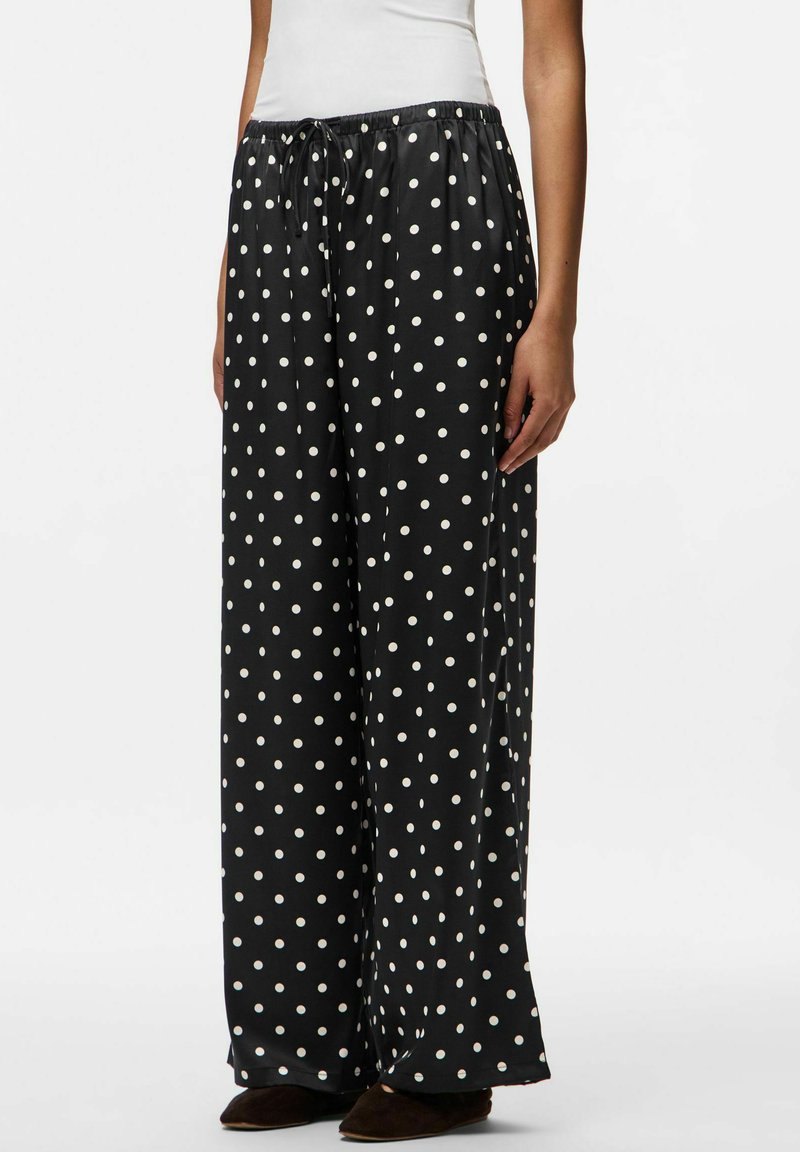 Melni, plati bikses ar auklu viduklī, ar baltu punktiņu rakstu un gludu, spīdīgu auduma tekstūru.