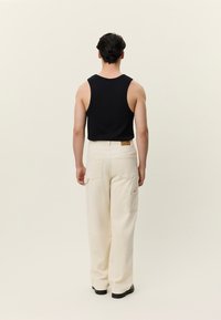 Crna pamučna majica bez rukava i kremaste široke cargo hlače s džepovima. Značajna tekstura tkanine, vidljivi šavovi i etiketa na pojasu.