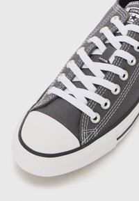 Gray canvas sneaker with white rubber toe cap and sole. Features white laces, metallic eyelets, and contrasting stitching details.