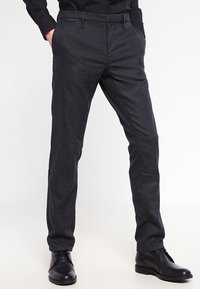 Mörkgrå mönstrade byxor med slim fit, tillverkade av ett vävt tyg; har sidofickor och en platt framsida. Svarta skor fulländar outfiten.