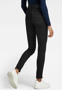 Smala svarta denimjeans med hög midja, diskret sömnad och två bakfickor, i kombination med vita sneakers.