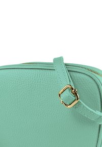 Licht turquoise leren tas met een getextureerde afwerking, voorzien van een gouden rits en hardware. Inclusief een bijpassende draagband.