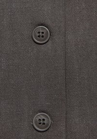 Twee donkergrijze knoppen genaaid op gestructureerde grijze stof, verticaal uitgelijnd met zichtbare stitches en details van de weving van de stof.