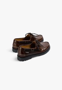 Zapatos de barco de cuero marrón con una textura suave, punta redonda, cordones de piel cruda, costuras en contraste y una suela de goma negra duradera.