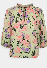 Blouse vert clair avec imprimé floral rose et violet, manches bouffantes 3/4 et petit col à volants avec une encolure fendue à l'avant.