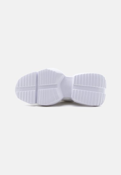 Semelle de chaussure blanche avec des rainures profondes et des crampons larges, présentée à plat sur un fond gris.