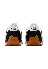 Baskets Nike en noir et blanc avec un talon en suede noir texturé, une tige en mesh blanche et une semelle en caoutchouc présentant un motif en zigzag.