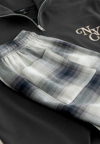 Czarna bluza na zamek z logo "NY", w połączeniu z białymi i szarymi szortami w kratę z elastycznym pasem i teksturowanym materiałem.