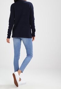 Marineblauer gestrickter Pullover mit langen Ärmeln, kombiniert mit hellblauen Skinny-Jeans und weißen Sneakers mit strukturierten Sohlen.