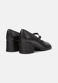 Pair of black leather Mary Jane shoes with rounded block heels and adjustable straps on a white background.