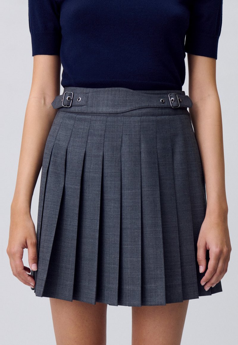 Falda gris con pliegues de tejido texturizado, con una cintura ajustada y un detalle de hebilla en el cinturón. Diseño clásico con líneas nítidas.