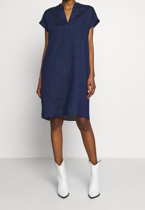 Navy linen shift dress with a V-neckline and short sleeves, featuring a relaxed fit and a curved hem. Styled with white cowboy boots.