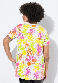 Camiseta de manga corta blanca con un vibrante patrón de salpicaduras en rosa, amarillo, verde y naranja. Corte holgado con un escote redondeado.