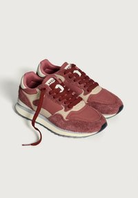 Ett par röda och beige mocka- och tygsneakers med vinröda snören, vita mellansulor och grå yttersulor på en vit bakgrund.