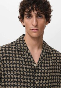 Korte mouwen overhemd in zwarte stof met een herhalend geometrisch patroon in beige, bruin en gouden accenten; met omvouwbare kraag en knopen aan de voorkant.