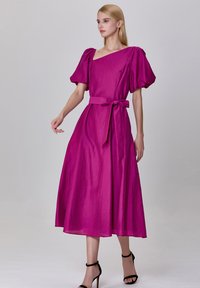 Robe maxi fuchsia avec manches bouffantes, un décolleté carré et une taille ceinturée. Fabriquée en tissu texturé, s'évasant en une jupe ample.