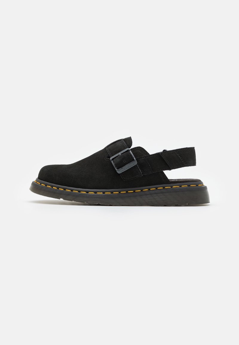 Chaussure slingback en daim noir avec bride à boucle, semelle épaisse en caoutchouc et surpiqûres jaunes le long du bord de la semelle, sur fond uni.