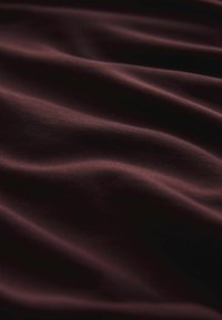 Burgundia kangas, millel on sile tekstuur, näidates pehmeid, voolavaid laineid ja õrna läiget, viidates kergesti venivale materjalile.