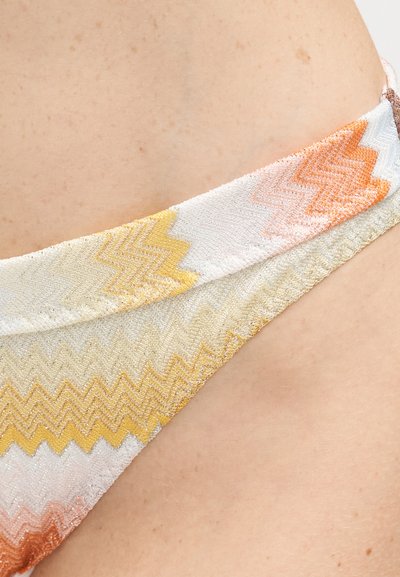 Gros plan sur un tissu à motifs en zigzag jaunes, blancs, orange et beige sur la peau d'une personne.