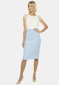 Jasnoniebieska spódnica ołówkowa o gładkiej teksturze i dopasowanym kroju, zestawiona z białą bluzką z przezroczystymi wstawkami na ramionach w kropki.
