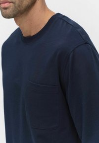 T-paita syvänsinisestä puuvillasta, jossa on pyöreä pääntie, lyhyet hihat ja vasemmalla puolella rintatasku. Silkkinen pinta ja yksinkertaiset muotoiluyksityiskohdat.