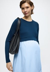 Μπλε μπλούζα με μακριά μανίκια και κομμένο σχεδιασμό, σε συνδυασμό με ανοιχτό μπλε ριγέ φόρεμα. Μαύρη δερμάτινη τσάντα ώμου τονίζει την εμφάνιση.