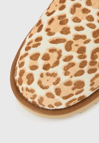 Παπούτσι slip-on με τύπωμα λεοπάρδαλης και απαλή υφή από συνθετική γούνα σε αποχρώσεις καφέ και κρεμ. Διαθέτει καστανή λαστιχένια σόλα και ραφές κατά μήκος της άκρης.