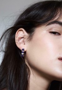 Lila Edelsteinohrstecker mit silbernen Akzenten, die ein lineares Design und eine polierte Oberfläche aufweisen, präsentiert am Ohr eines Modells vor neutralem Hintergrund.