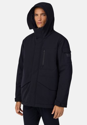 Chaqueta aislante de color azul marino con un alto cuello y capucha, que cuenta con bolsillos en el pecho y en los laterales con cremallera, y un diseño estructurado y moderno.