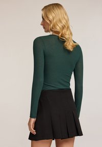 Vihreä pitkähiha toppi, joka on valmistettu läpinäkyvästä materiaalista, yhdistetty mustaan viistoon hameeseen. Toppi istuu tiukasti, siinä on pyöreä pääntie ja hieno kiilto.