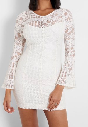 Vestido blanco de encaje con mangas largas acampanadas, que presenta una mezcla de patrones florales y geométricos, silueta ajustada y escote redondo.