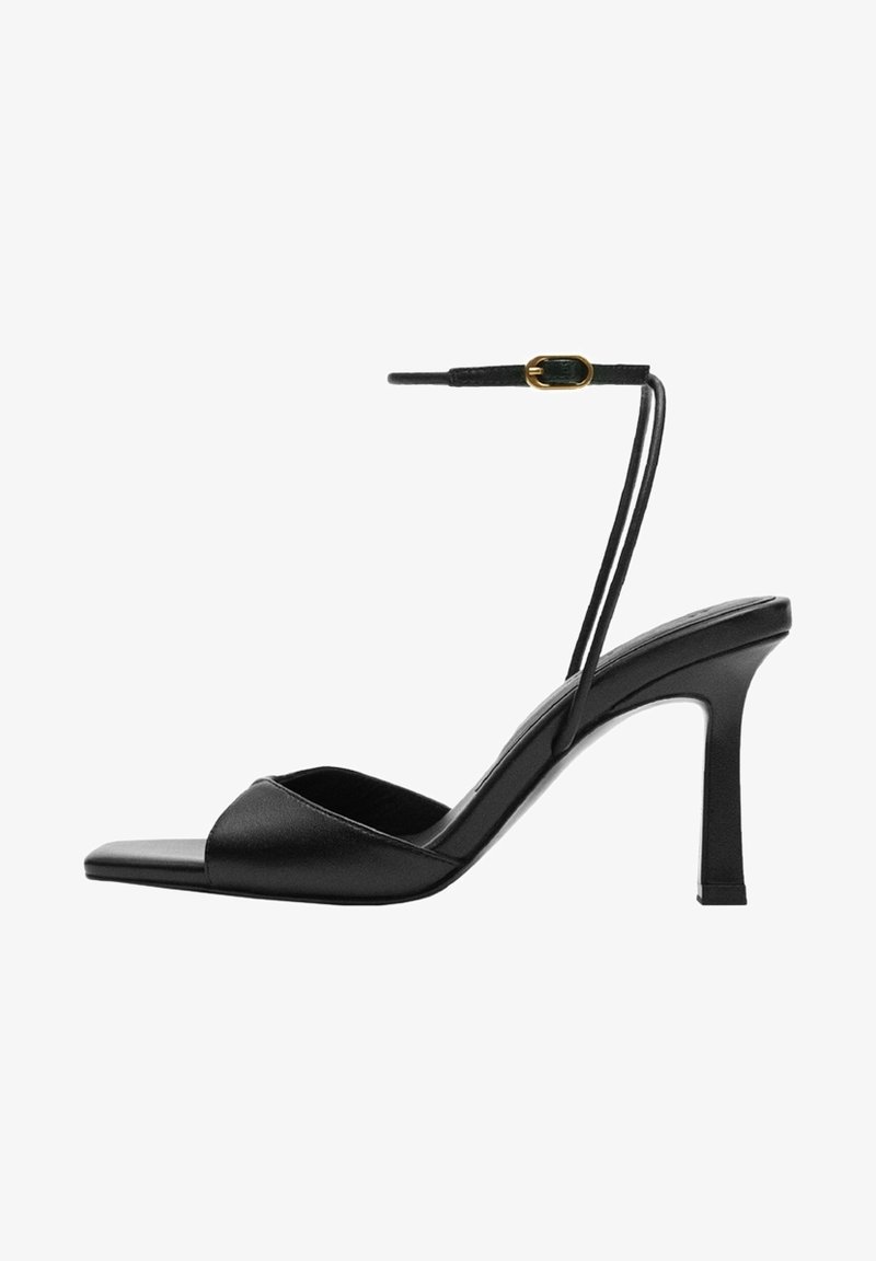 Sandale à talon haut noire avec fine bride autour de la cheville et boucle dorée, bout ouvert, et design à bout carré sur fond blanc.