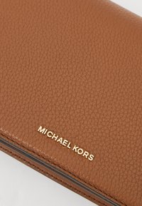 Bruine leren portemonnee met een gestructureerd oppervlak, voorzien van het gouden 'MICHAEL KORS'-logo. Het slanke ontwerp en de subtiele stikdetails maken de look compleet.