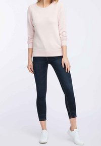 Sweat-shirt rose clair à manches longues, encolure ronde et ourlet côtelé, associé à un jean skinny foncé et des baskets blanches.