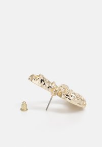 Guldtonade örhängen med en texturerad vågig design. Utrustad med en metallpinne och en avtagbar baksida. Glansig yta med accentdetaljer.