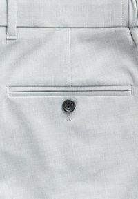 Hellgraue maßgeschneiderte Hose mit glatter Textur, flacher Vorderseite und einer einzelnen Gesäßtasche mit einem schwarzen Knopfdetail.