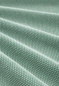 Texturiertes Gewebe in Grün mit einem weißen gepunkteten Muster, das eine weiche, gewebte Oberfläche zeigt, die Tiefe und visuelles Interesse schafft.
