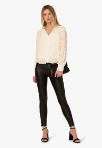 Cream blouse with textured floral pattern, button front, and long sleeves. Paired with shiny black leggings and black heeled sandals.