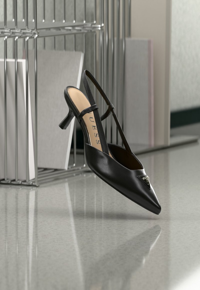 Μαύρο γοβάκι με λουράκι στο πίσω μέρος, ψηλό τακούνι kitten, μυτερή μύτη και μεταλλική λεπτομέρεια με λογότυπο, να αιωρείται κοντά σε ανακλαστική επιφάνεια και μεταλλική σχάρα με χαρτιά.