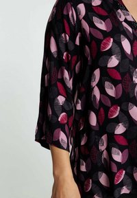 Haut en tissu noir avec un motif de feuilles dans des nuances de rose et de bordeaux, col en V et manches trois-quarts.