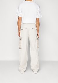Béžové cargo kalhoty s bočními kapsami, volným střihem, žebrovaným pasem a rovnými nohavicemi, doplněné o jednoduché bílé tričko.